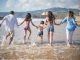 A family having fun running into the ocean on a sunny beach day in Portugal. Joyful and carefree moments.