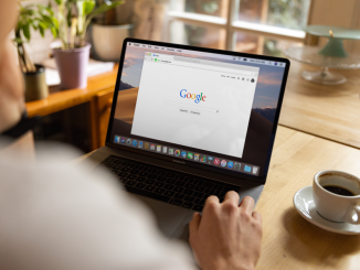 An adult using a laptop indoors, browsing Google at a wooden table with coffee.