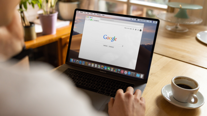 An adult using a laptop indoors, browsing Google at a wooden table with coffee.